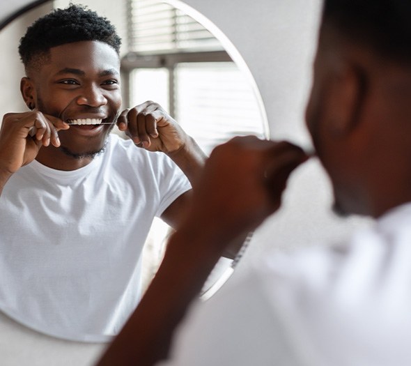 Man smiling while flossing in bathroom