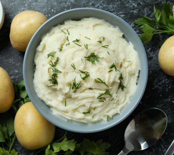 A bowl of mashed potatoes next to spoons